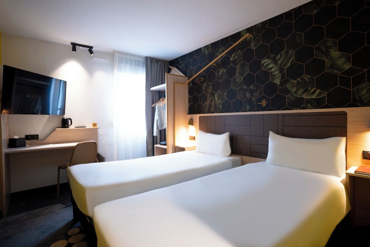 Habitación de hotel con dos camas, un escritorio, una silla, un televisor y zona de ducha.