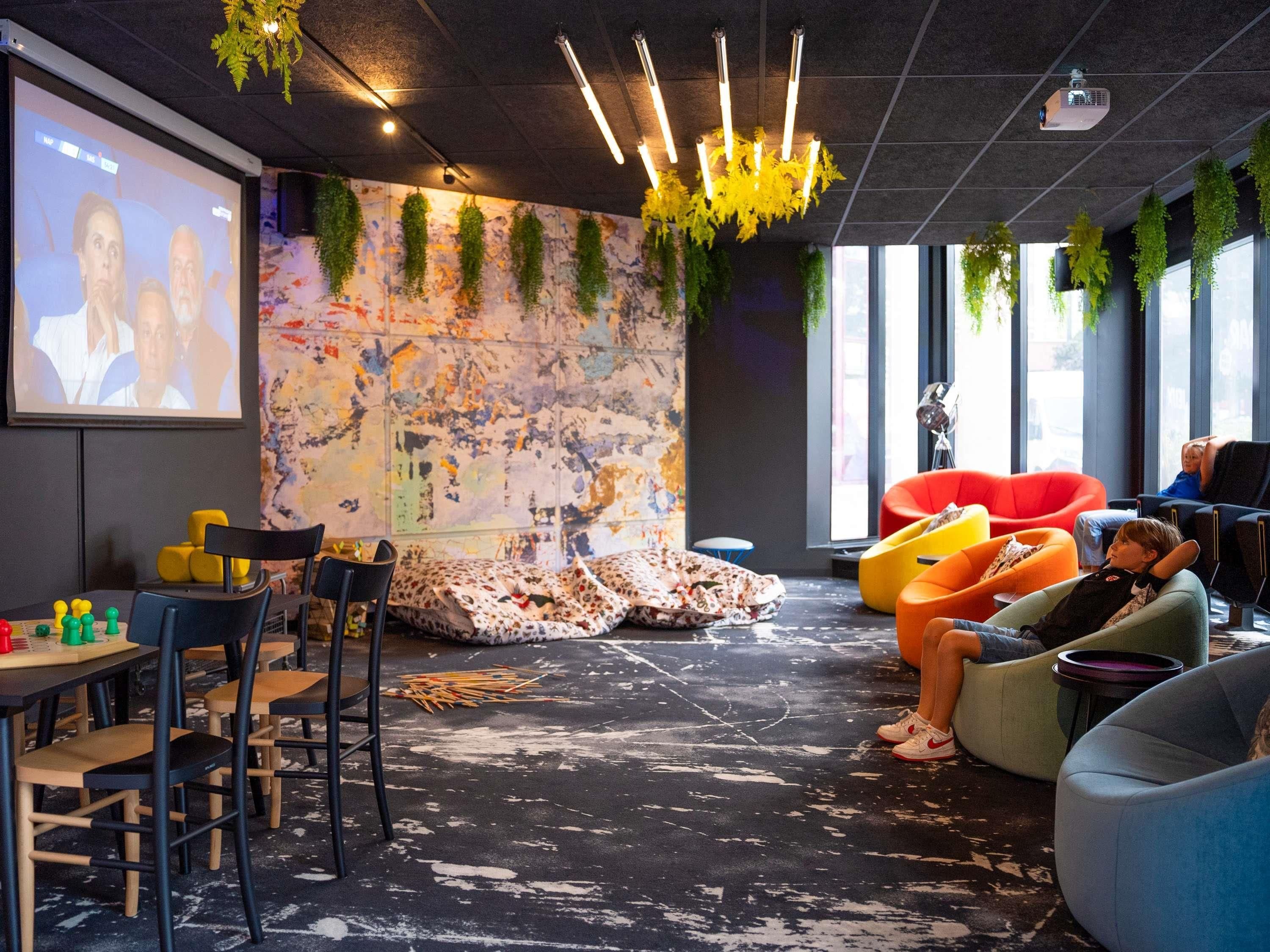 Un espace de détente moderne doté d’un écran de projection, de différents types de sièges et d’un mur orné d’une fresque à motifs.