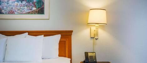 Una habitación de hotel con una cama, una mesita de noche con lámpara y un cuadro en la pared.