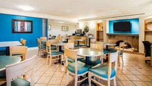A hotel lobby with multiple dining tables and chairs, a fireplace, a television mounted on the wall, and framed artwork on the walls. - La Quinta Inn by Wyndham Norfolk Virginia Beach (Virginia Beach)