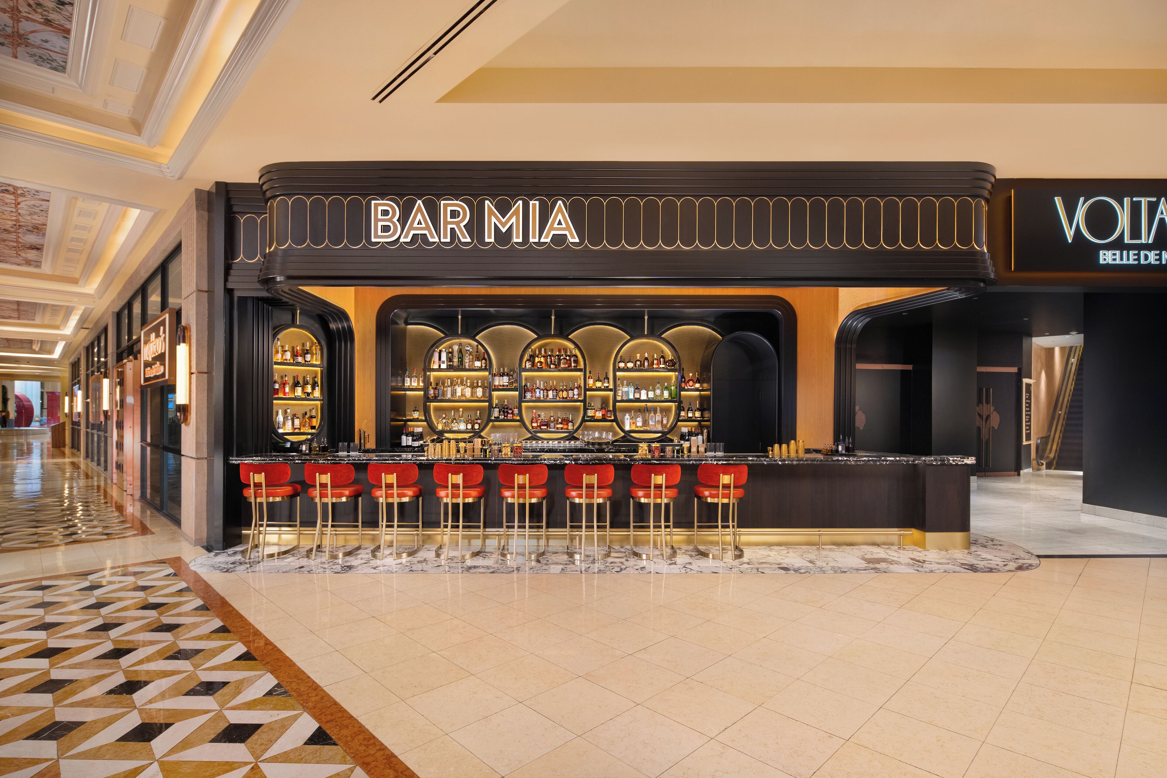 Un bar appelé BAR MIA, au design moderne, avec un comptoir doté de tabourets et une étagère où sont exposées les bouteilles.