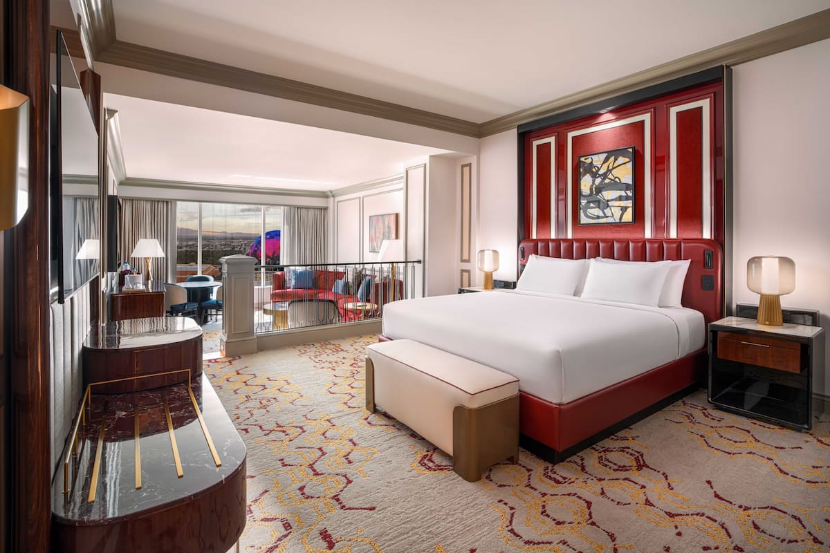 A hotel room with a large bed, a desk, a chair, a sofa, a large window, and a view of the city.