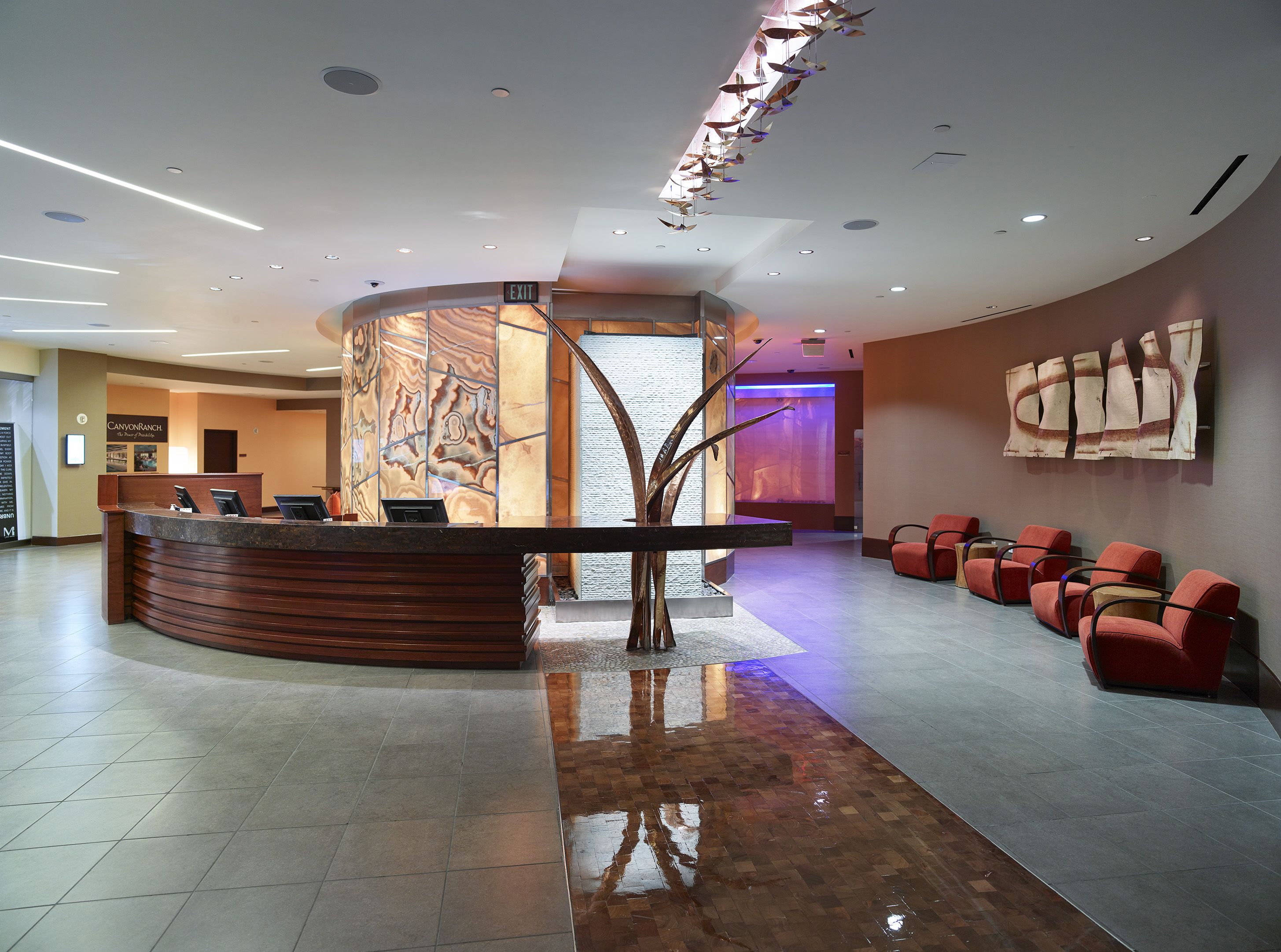 A modern reception area with a curved desk, a seating area with red chairs, and a large abstract wall art piece.
