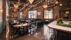 A restaurant with multiple dining tables and chairs, chandeliers, and large windows.