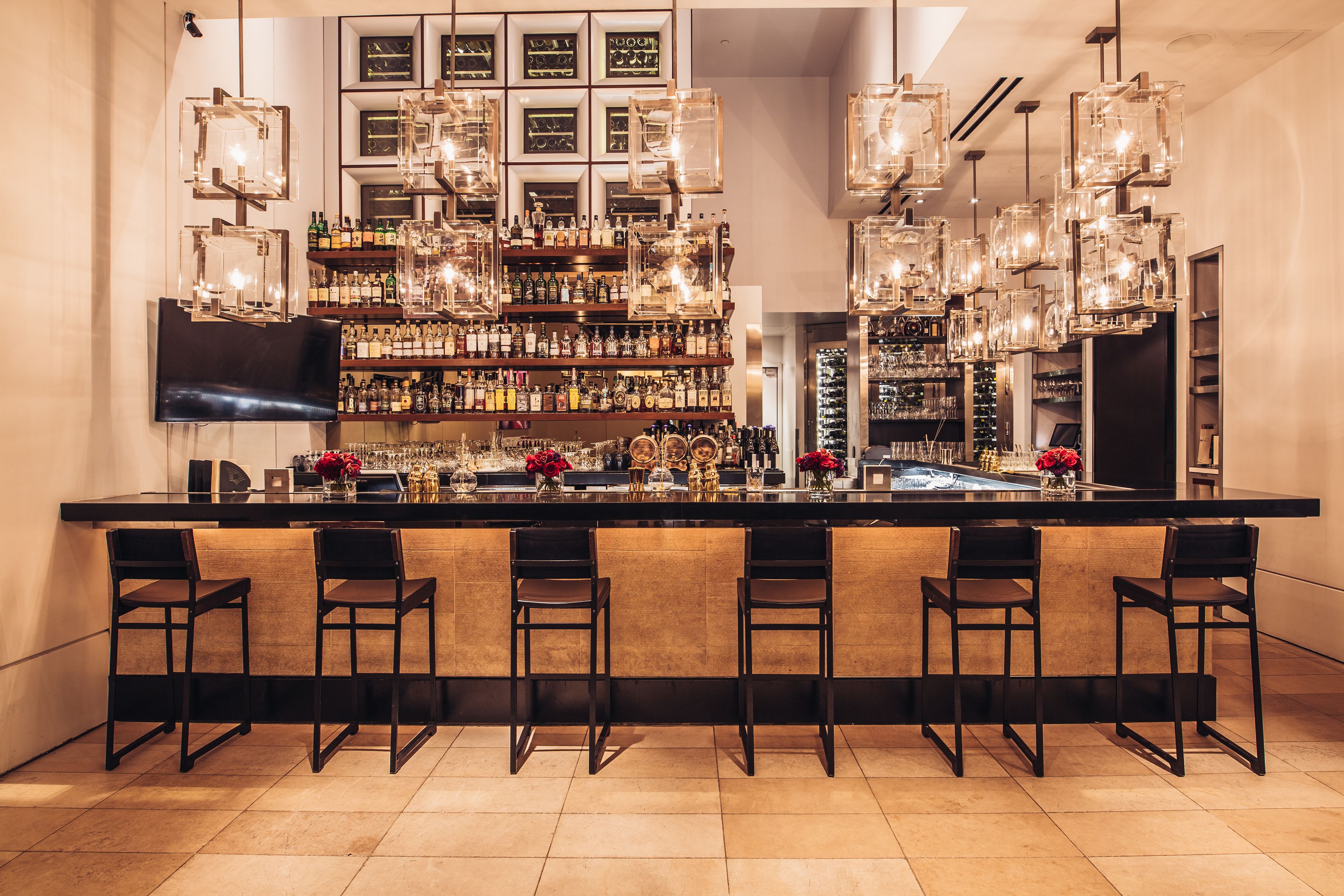 A bar area with a long counter, multiple hanging light fixtures, and a variety of bottles and glasses on shelves.