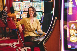 A woman seated at a slot machine, holding a drink.