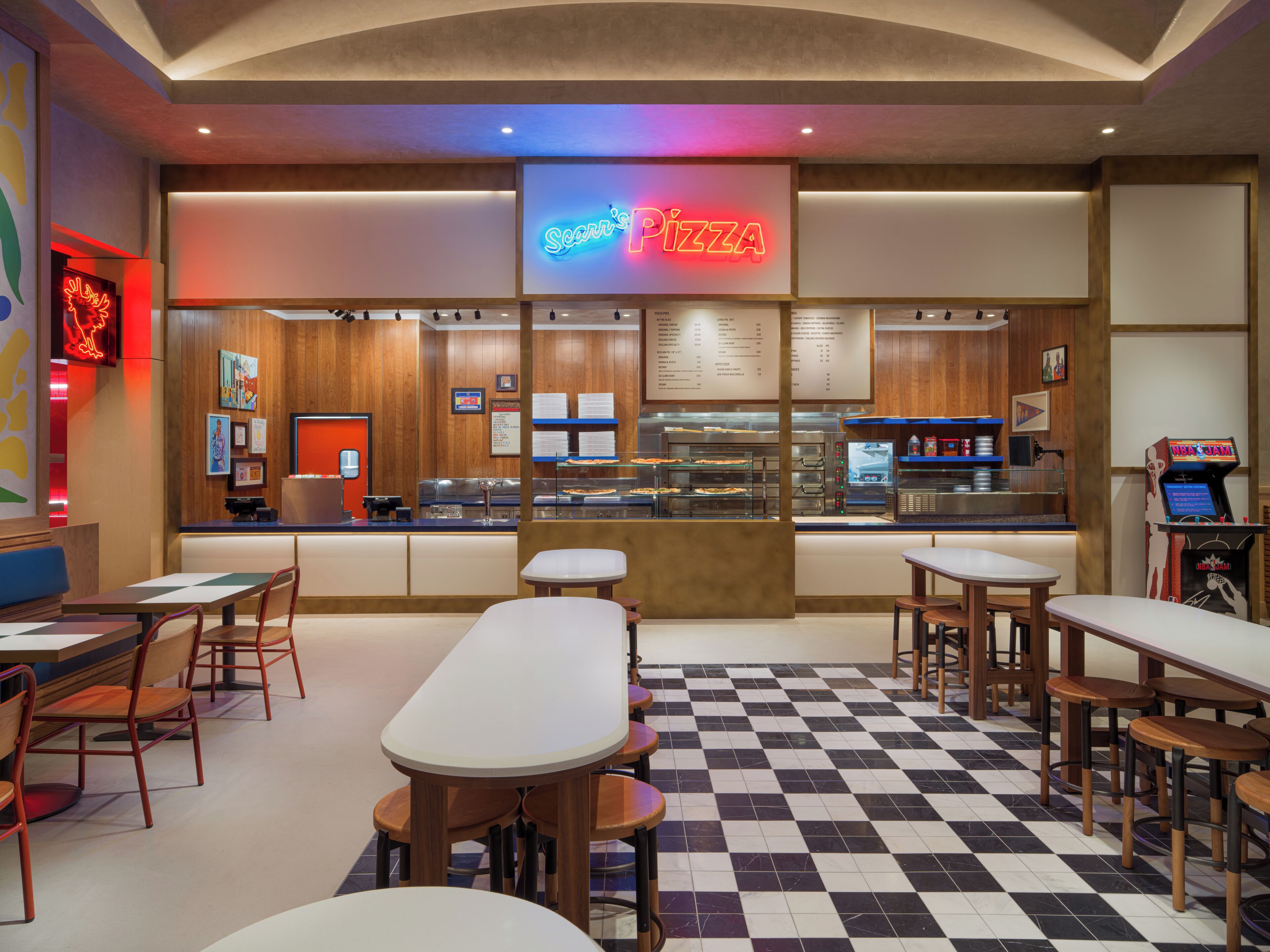 Het interieur van een pizzarestaurant met een neonbord, een geruit vloertje en een zithoek.