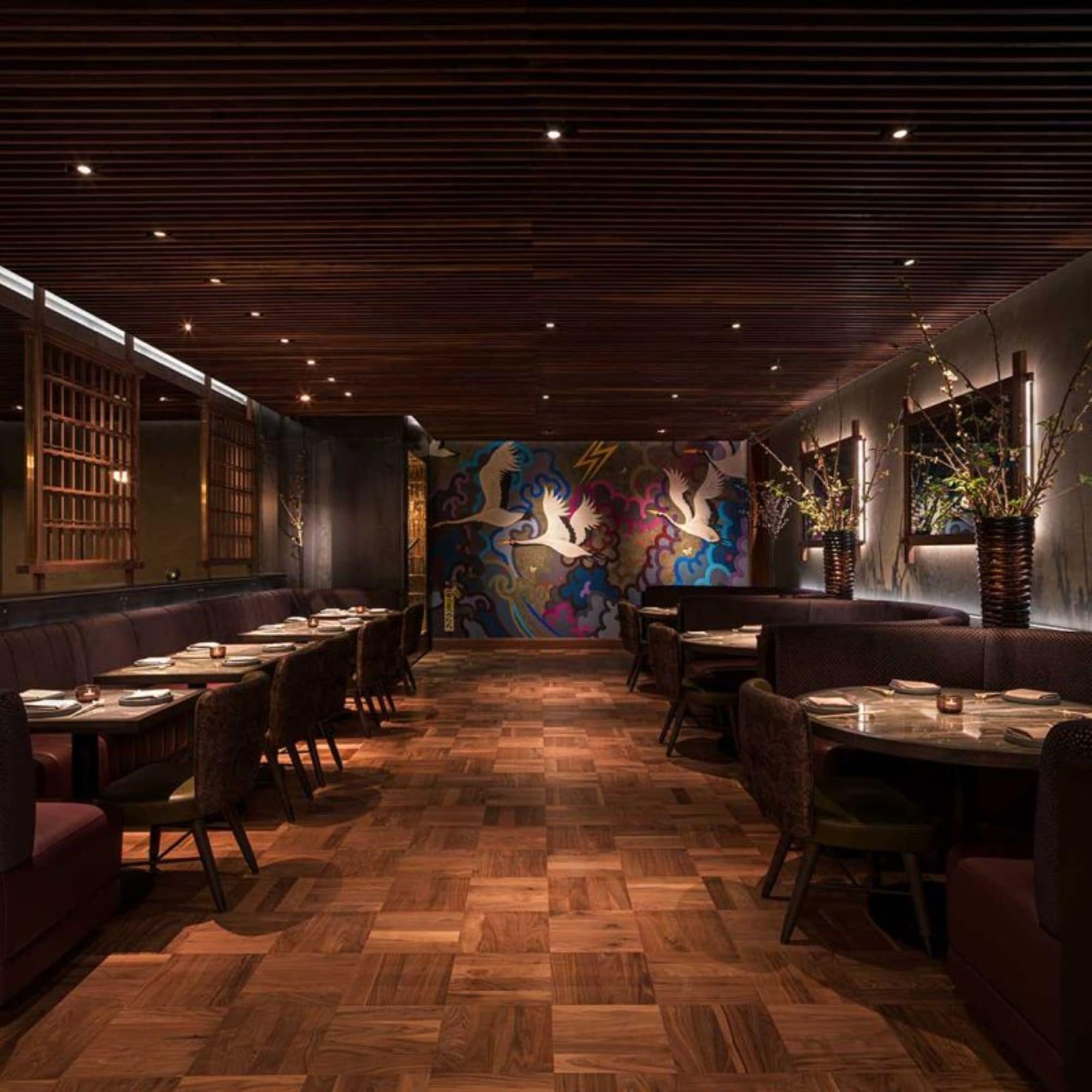 A restaurant interior with wooden flooring, booths, and a colorful mural on the back wall.