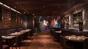 Een restaurantinterieur met houten vloeren, zitjes en een kleurrijke muurschildering op de achterwand.