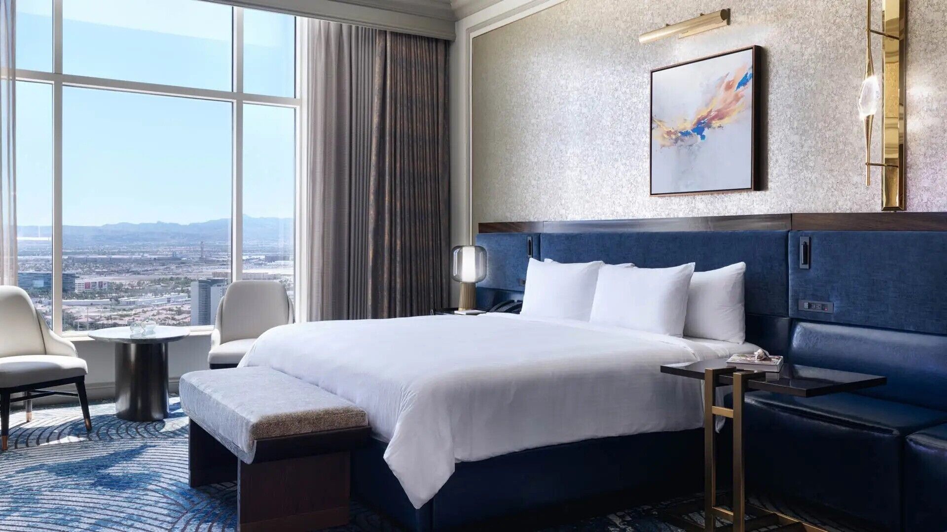 Una habitación de hotel con una cama grande, zona de estar, escritorio y vista a un paisaje urbano.