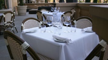 A table set for dining outdoors with wicker chairs, white tablecloths, and wine glasses.