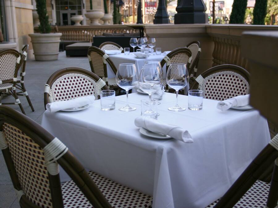 A table set for dining outdoors with wicker chairs, white tablecloths, and wine glasses.