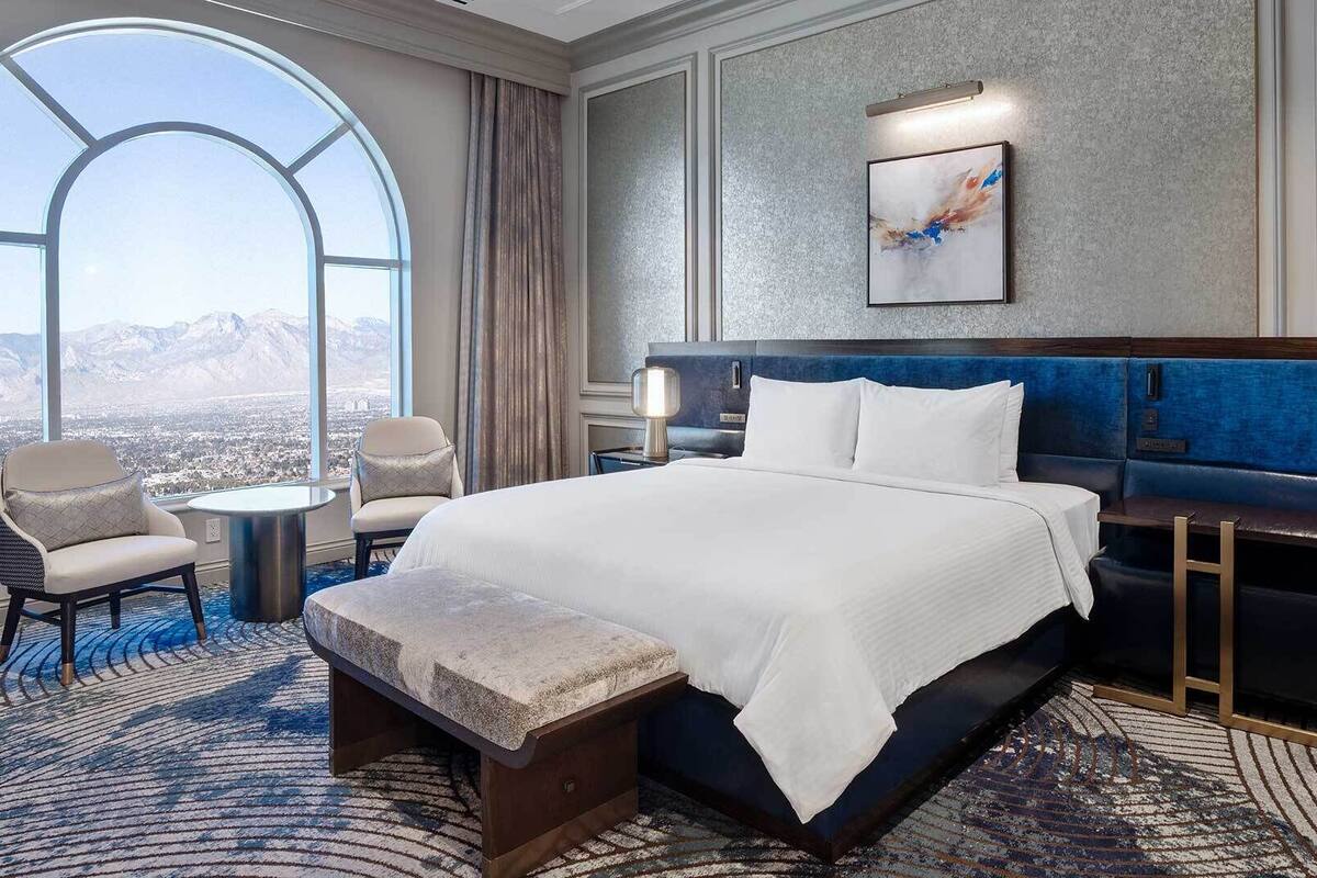 A hotel room with a large bed, a seating area with a view, and a painting on the wall.