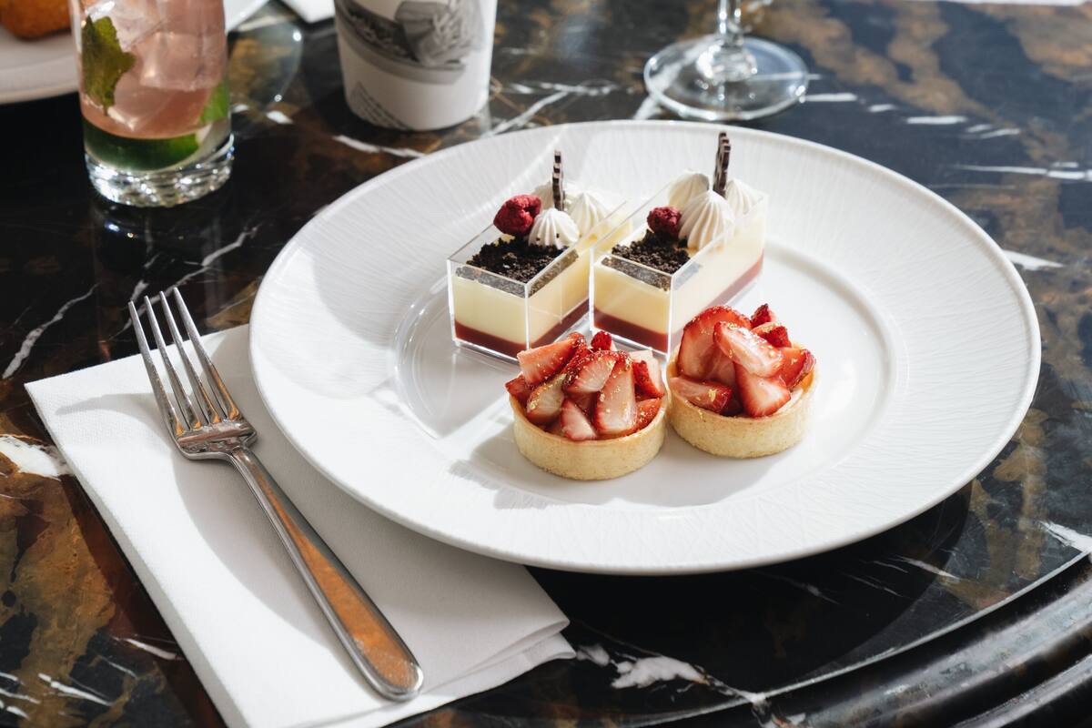 A dining table with a plate of desserts, a glass of water, a bottle of soda, and a napkin.