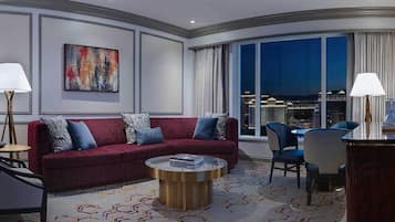 A modern hotel room with a red sofa, a round coffee table, and a large window offering a city view.