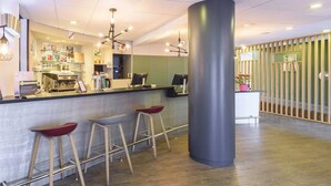 A reception area with a counter, stools, a large pillar, and a wooden floor. - B&B Hotel Toulouse Université (Toulouse)
