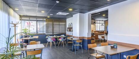 A modern restaurant interior with tables, chairs, and potted plants.