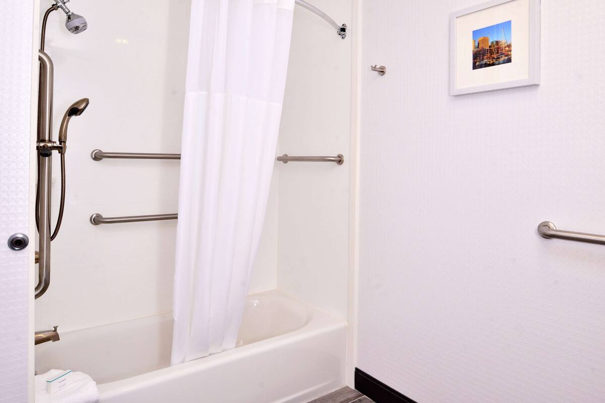 A bathroom with a bathtub, grab bars, a showerhead, and a framed picture on the wall.