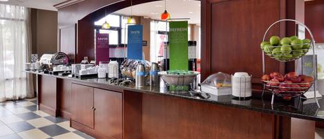 Zona de recepción de un hotel con mostrador de recepción, máquinas de café y un frutero.