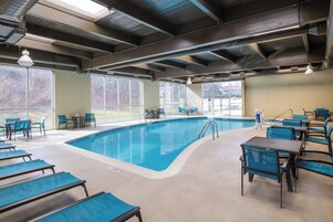 Zona de piscina con sillones de descanso y mesas, ventanas amplias y vistas al exterior.