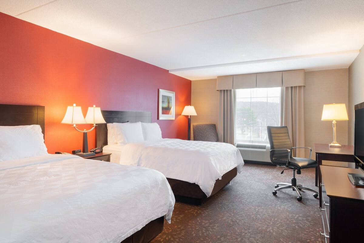 A hotel room with two beds, a desk, a chair, and a large window.