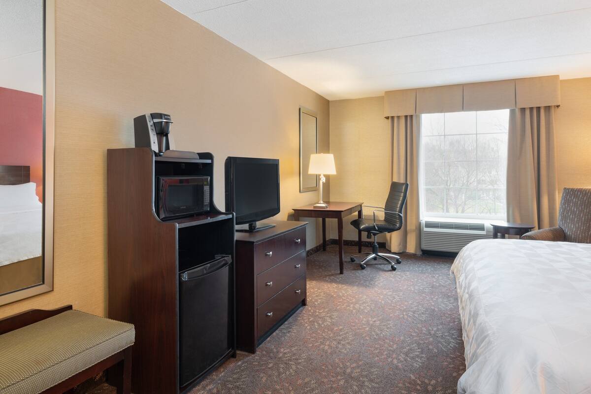 A hotel room with a bed, a desk with a lamp, a television, a coffee maker, and a chair.