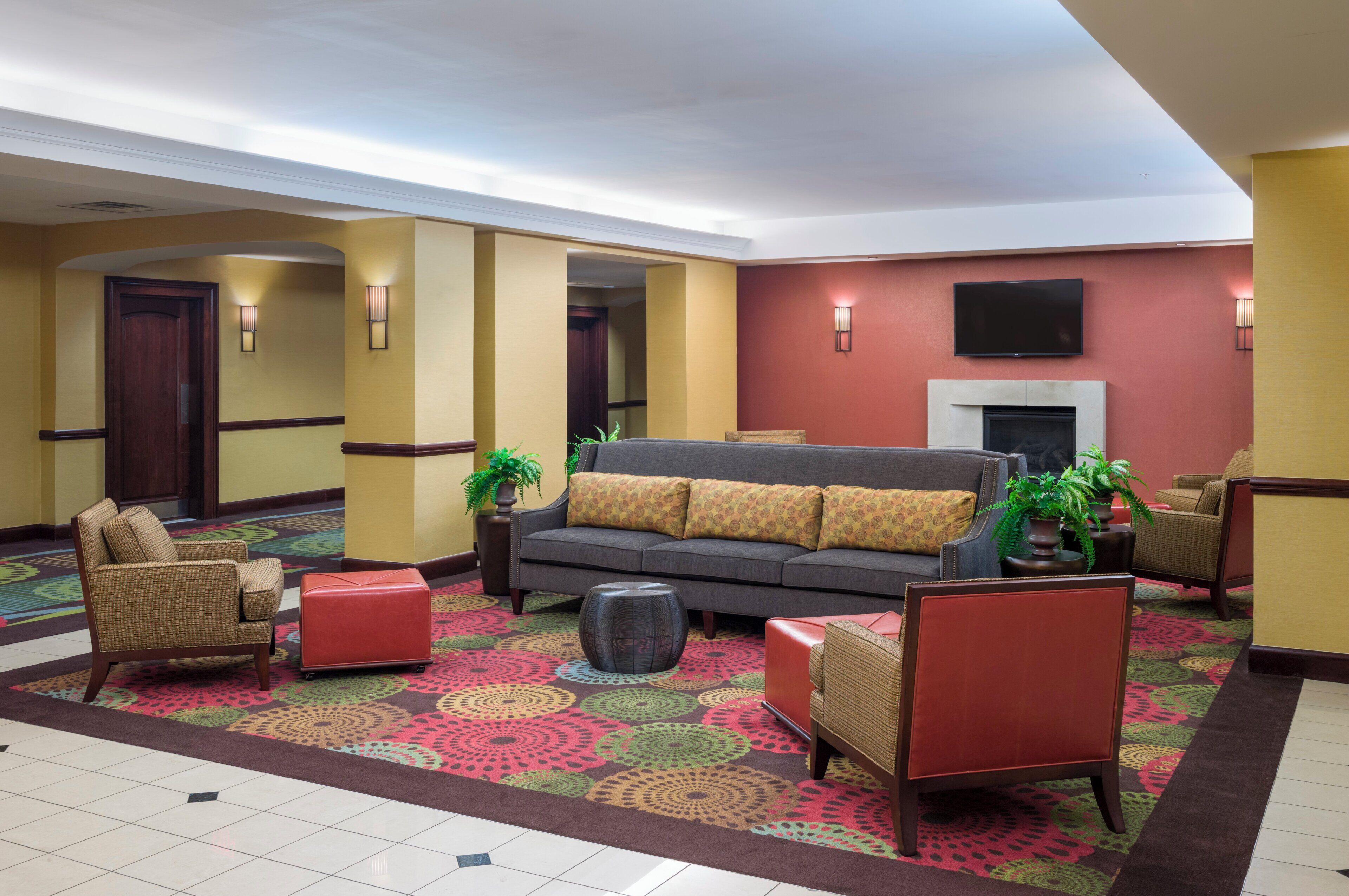 A hotel lobby with a sofa, armchairs, a fireplace, and a television mounted on the wall.