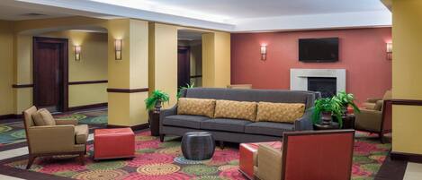 A hotel lobby with a sofa, armchairs, a fireplace, and a television mounted on the wall.