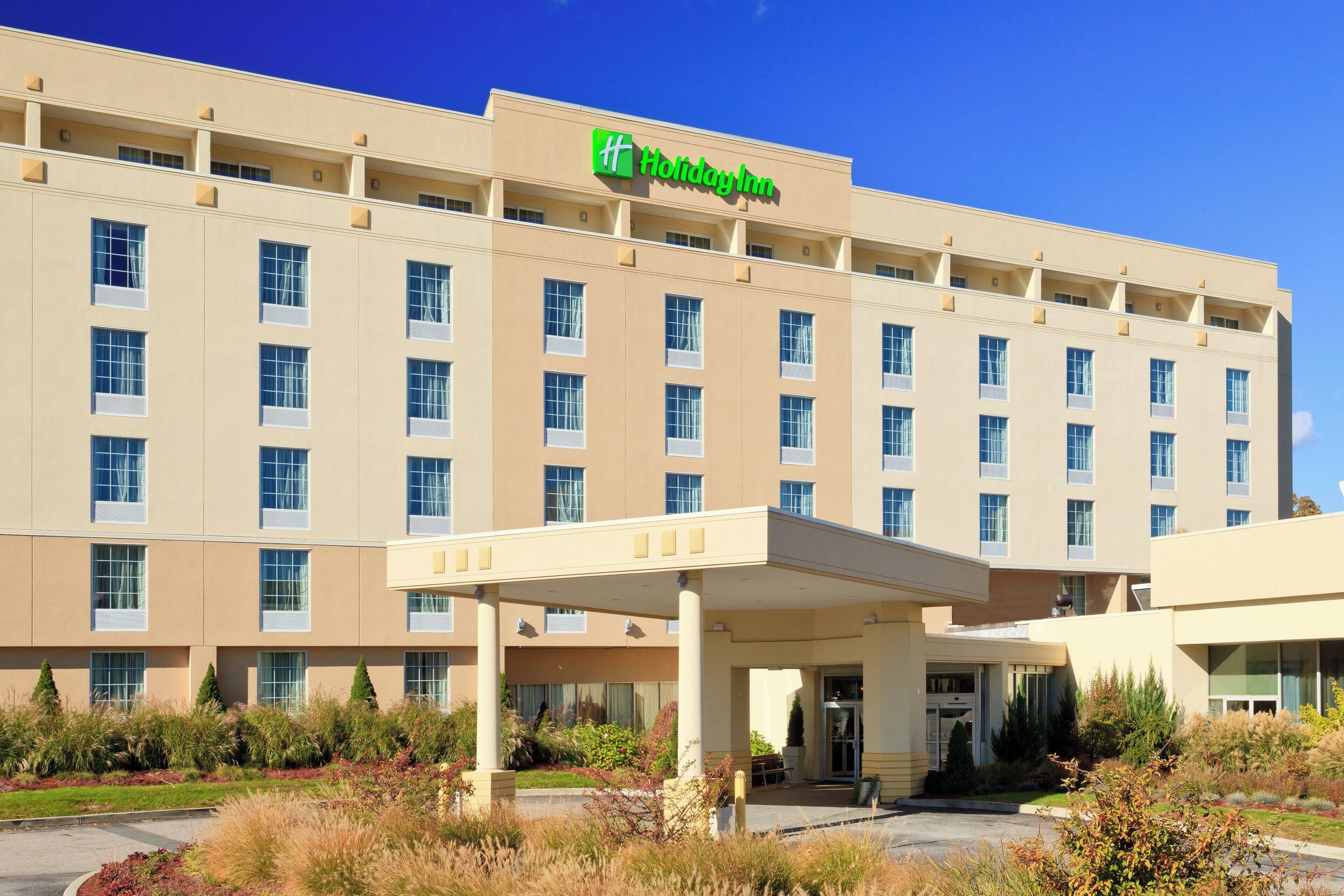 Un hotel Holiday Inn con un edificio grande, muchas ventanas y un área de entrada techada.