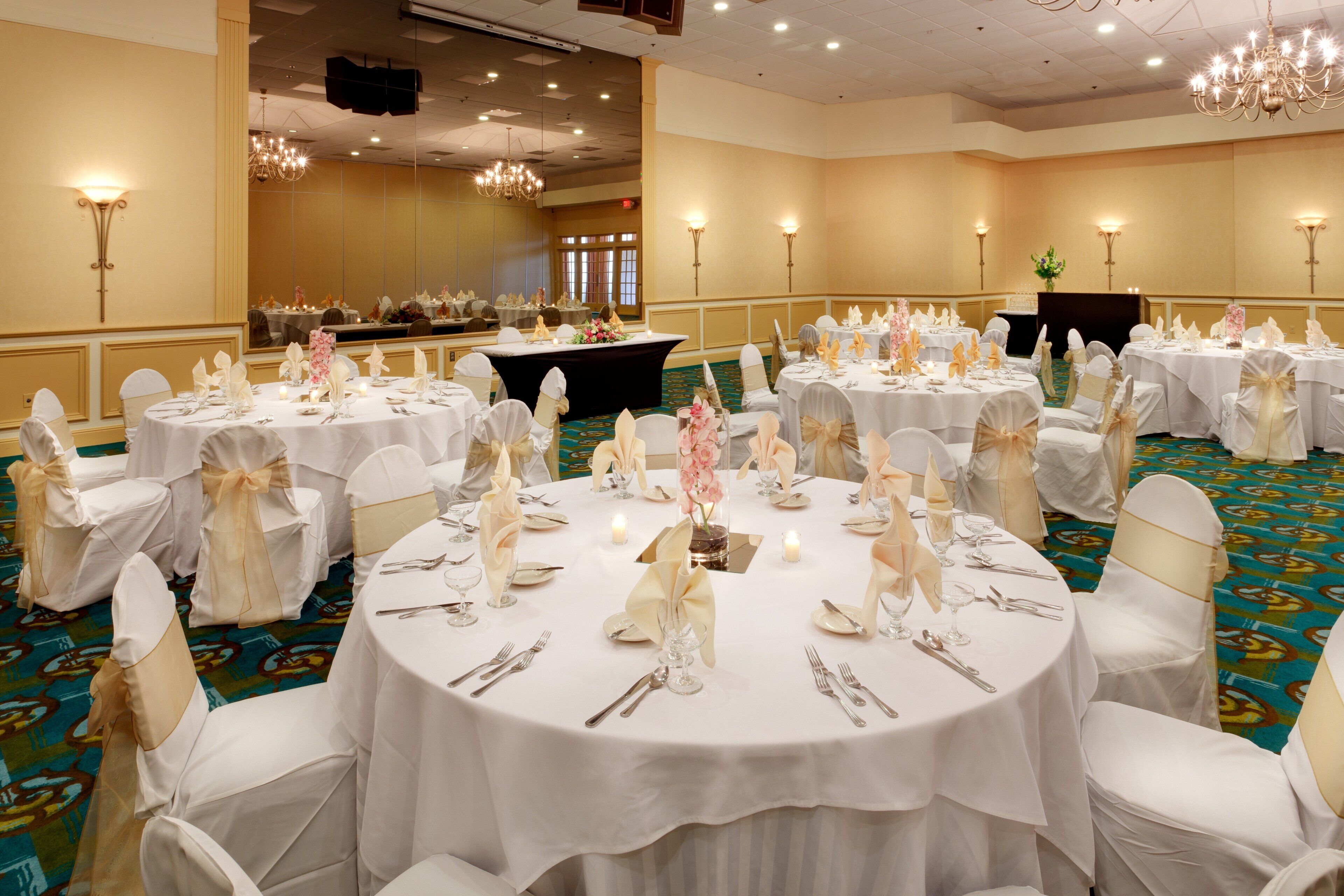 Un salón de banquetes con mesas redondas dispuestas para un evento formal, con manteles blancos, cubiertos de plata y centros de mesa florales.