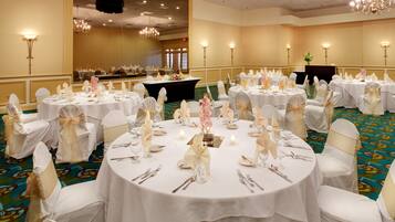 Un salón de banquetes con mesas redondas dispuestas para un evento formal, con manteles blancos, cubiertos de plata y centros de mesa florales.