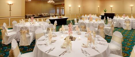 A banquet hall with round tables set for a formal event, featuring white tablecloths, silverware, and floral centerpieces.