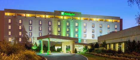 Een Holiday Inn hotel met een goed verlichte ingang, meerdere verdiepingen en een aangelegde oprit.