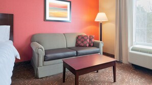 A hotel room with a grey sofa, a wooden coffee table, a framed picture on the wall, and a window with curtains. - Holiday Inn Norwich by IHG (Norwich)