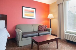 A hotel room with a grey sofa, a wooden coffee table, a framed picture on the wall, and a window with curtains. - Holiday Inn Norwich by IHG (Norwich)