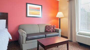 A hotel room with a sofa, a small table, a lamp, and a window with curtains.