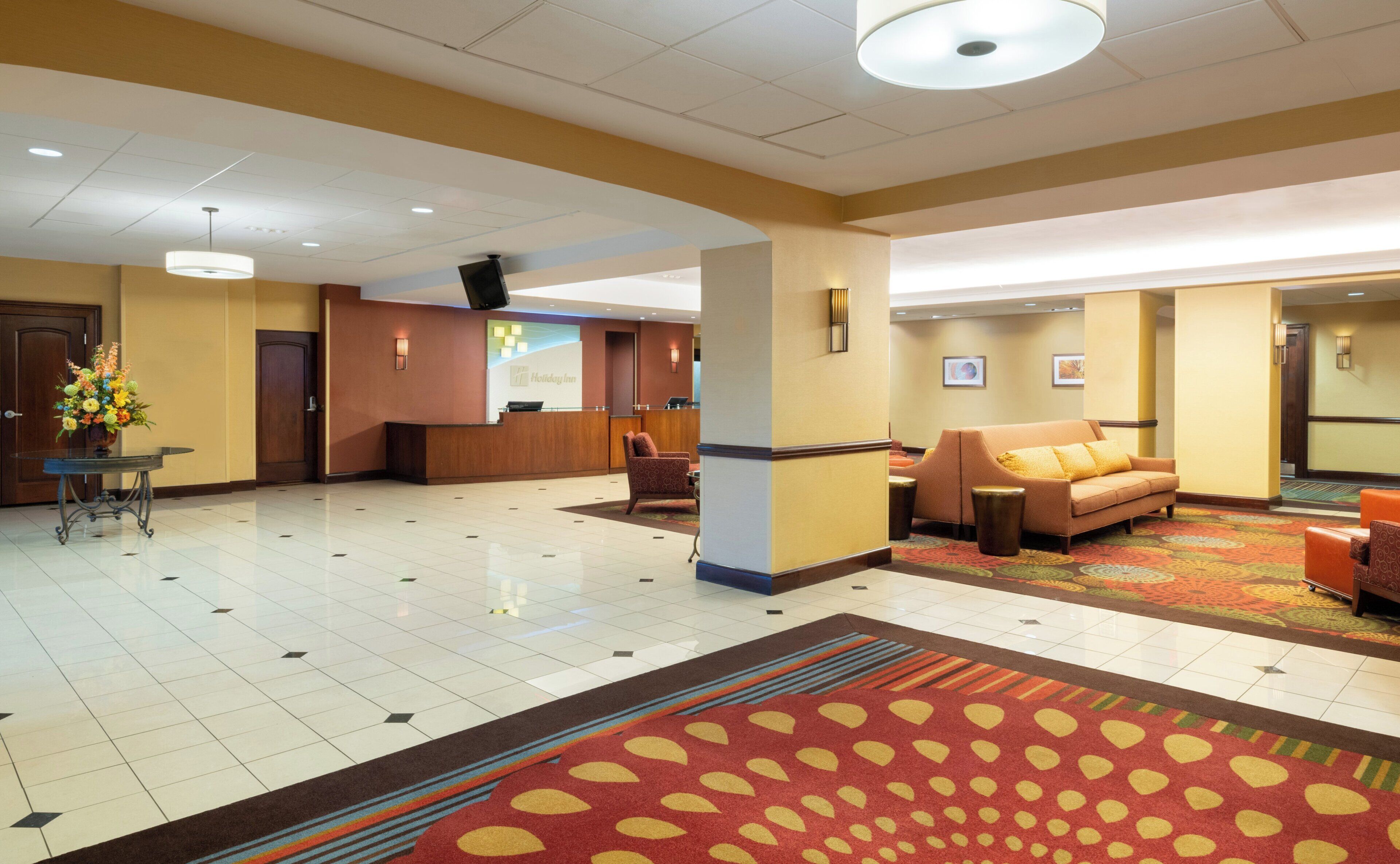 A hotel lobby with a reception desk, seating area, and a patterned carpet.