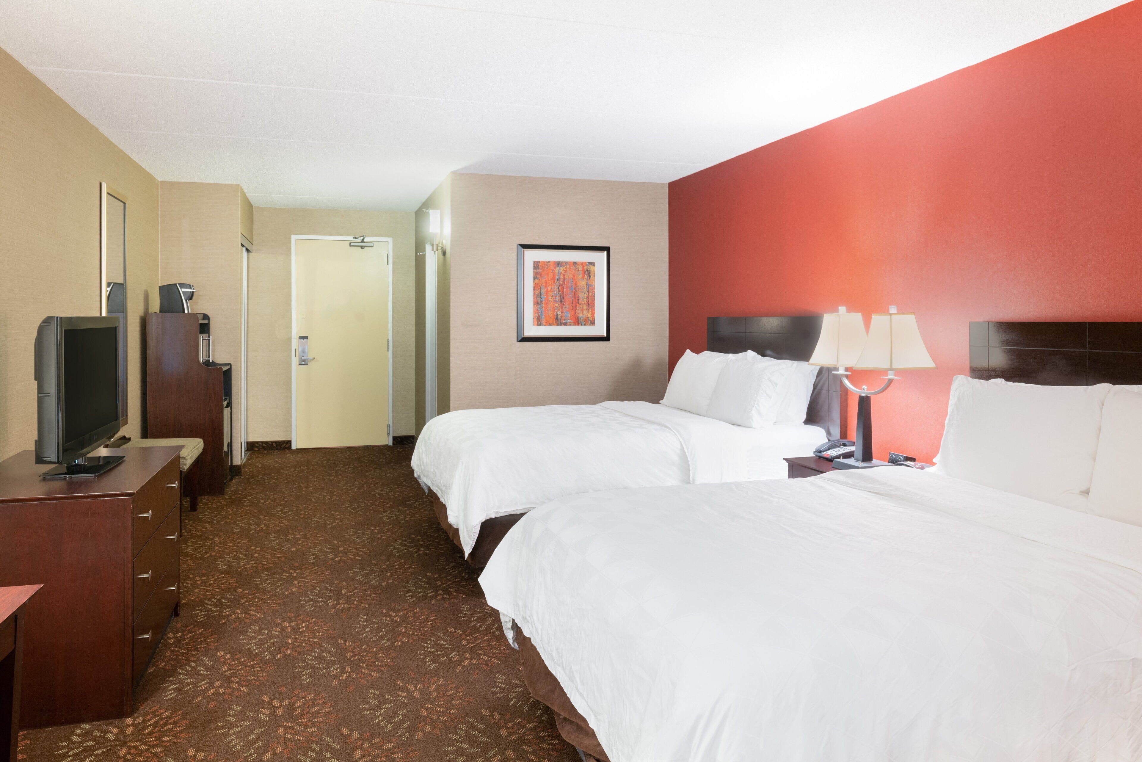 A hotel room with two beds, a desk with a television, and a door leading to a bathroom.