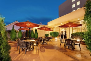 An outdoor patio area with tables and chairs, surrounded by greenery and umbrellas. - Holiday Inn Norwich by IHG (Norwich)