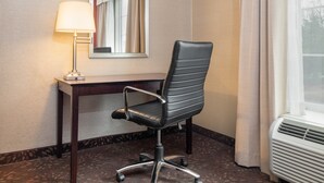 A hotel room with a desk, a chair, a lamp, a mirror, and an air conditioning unit. - Holiday Inn Norwich by IHG (Norwich)