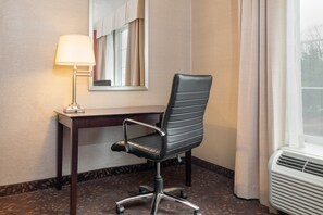 A hotel room with a desk, a chair, a lamp, a mirror, and an air conditioning unit. - Holiday Inn Norwich by IHG (Norwich)