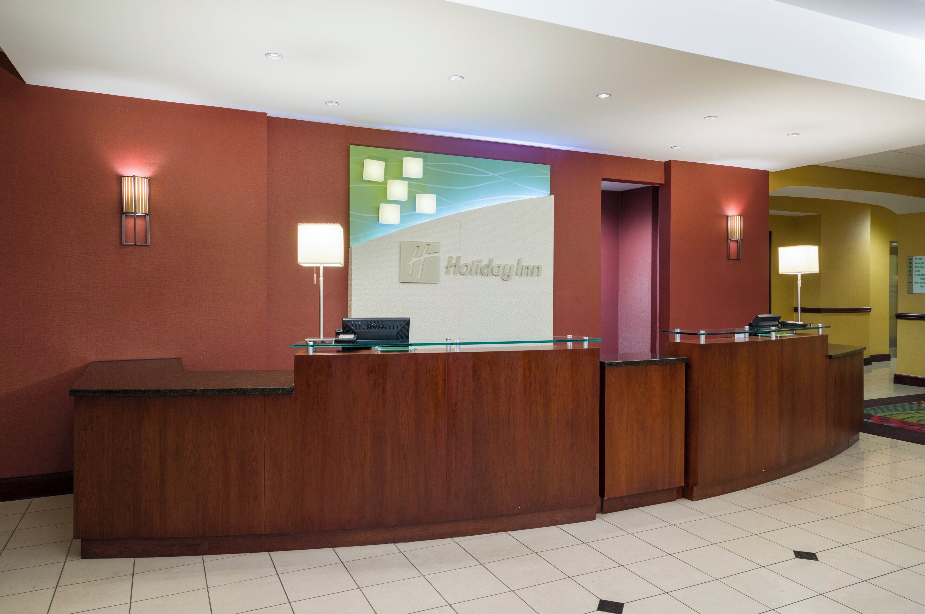 A reception desk with a Holiday Inn sign, a glass partition, and a reception area with a tiled floor.