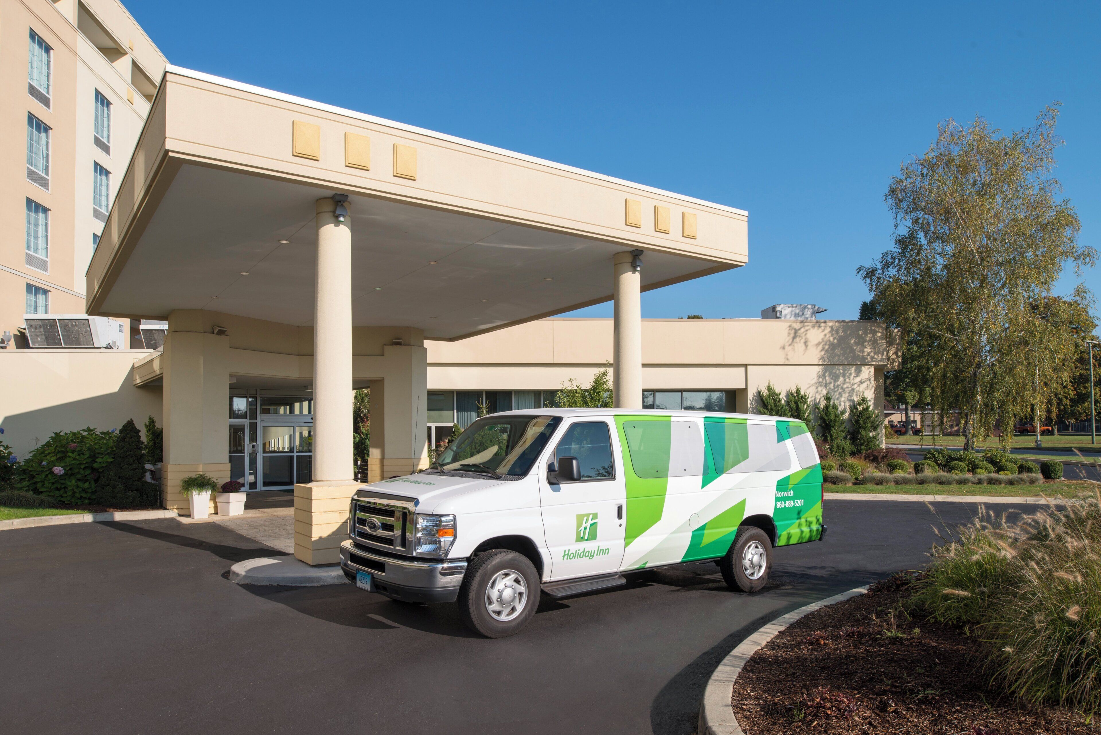 A white van with green accents parked in front of a building with a covered entrance and multiple columns.
