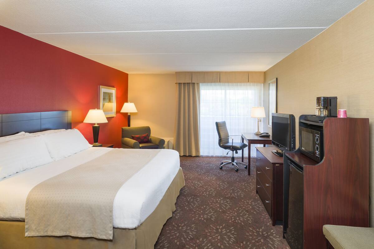 A hotel room with a large bed, two bedside tables with lamps, a desk with a television and coffee maker, and a chair.