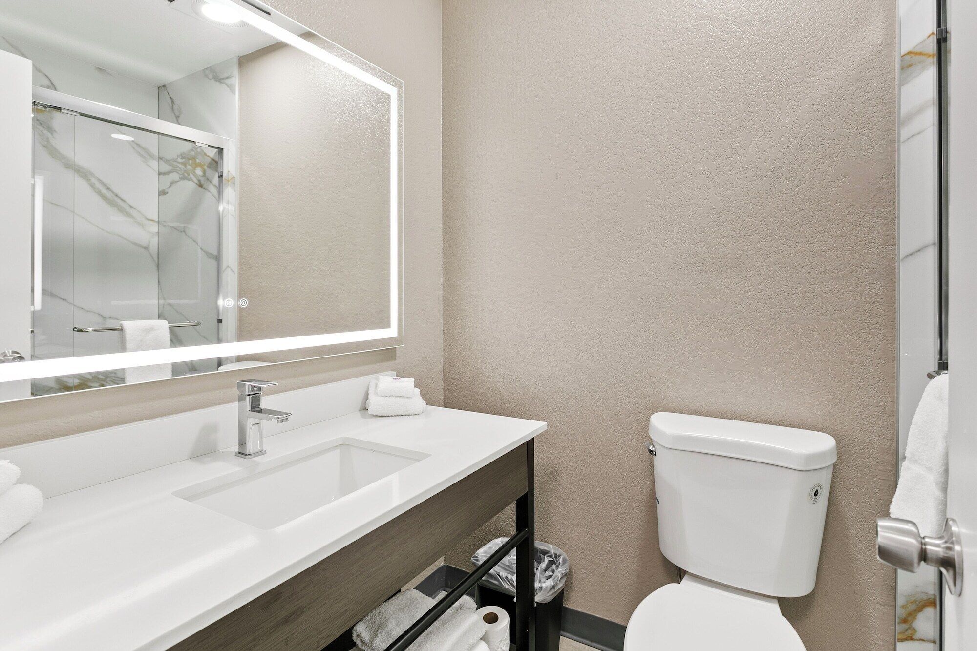 Un baño moderno con un espejo grande, un lavabo y un inodoro.