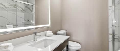 A modern bathroom with a marble-tiled shower enclosure, a white sink with a mirror, and a toilet.