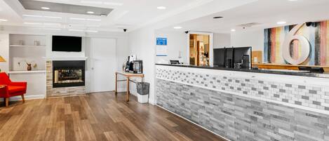 A reception area with a modern design, featuring a reception desk, a fireplace, and a large wall-mounted TV.