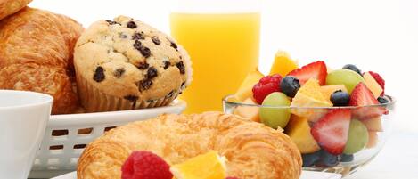 A breakfast setting with croissants, muffins, and a fruit bowl.