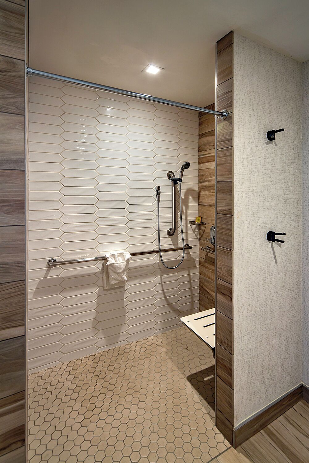 A modern bathroom with a glass shower enclosure, a wooden vanity, and a hexagonal tile floor.