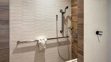 A modern bathroom with a glass shower enclosure, a wooden vanity, and a hexagonal tile floor.